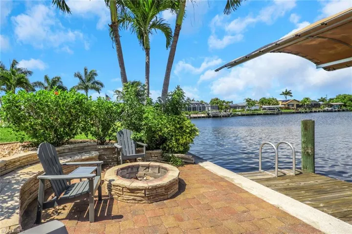 Waterside patio featuring a paver surface, built-in stone fire pit, and extensive landscaping