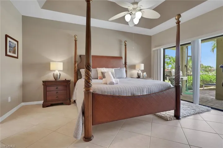 Spacious interior featuring a tray ceiling with a ceiling fan and recessed lighting, light-toned tile flooring, and sliding glass doors opening to an outdoor patio with palm trees