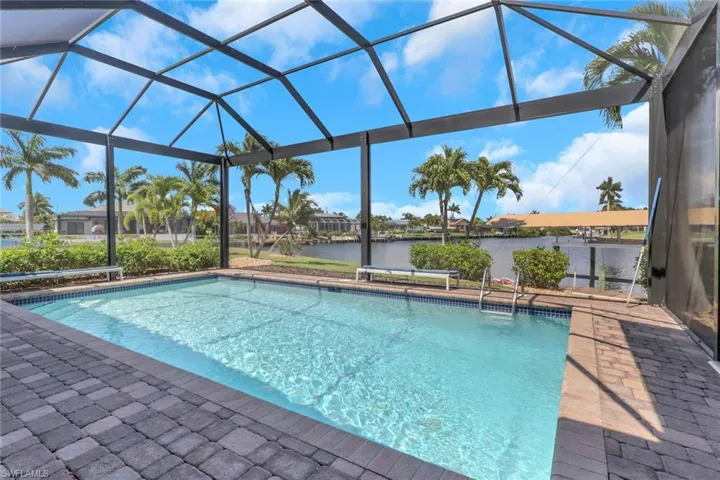 Screened outdoor pool area featuring a rectangular pool with integrated steps, surrounded by paver decking