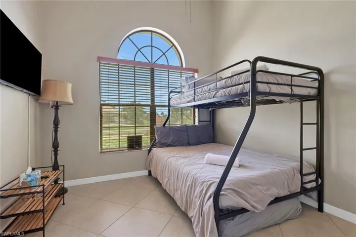 Room featuring a large arched window with horizontal blinds, neutral wall paint, tile flooring, and a flat-screen television mounted on the wall