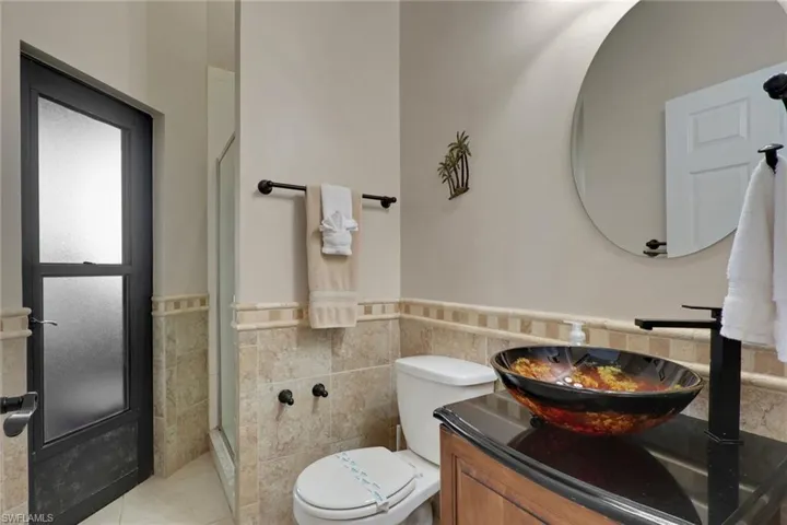 Bathroom featuring a vessel sink with an artistic bowl, dark granite countertop, wood-finish vanity, and a circular mirror
