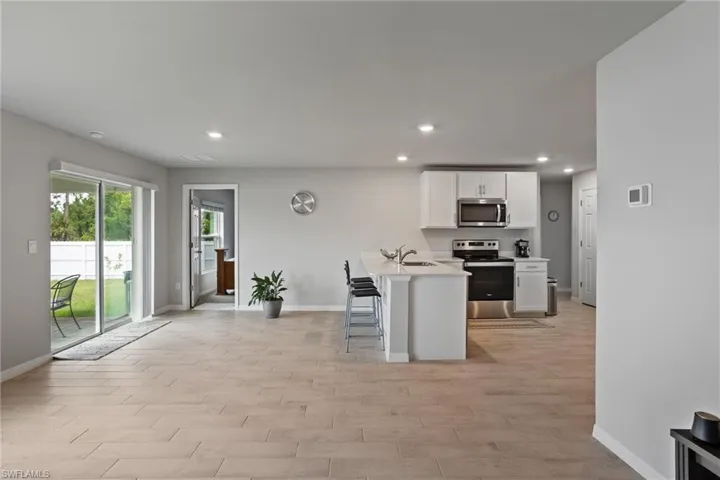 Kitchen with appliances with stainless steel finishes, baseboards, a sink, white cabinets, and light countertops