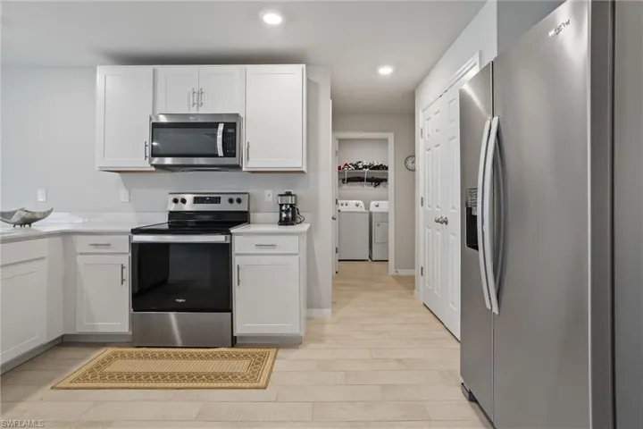 Kitchen with stainless steel appliances, washer and dryer, white cabinetry, light countertops, and recessed lighting