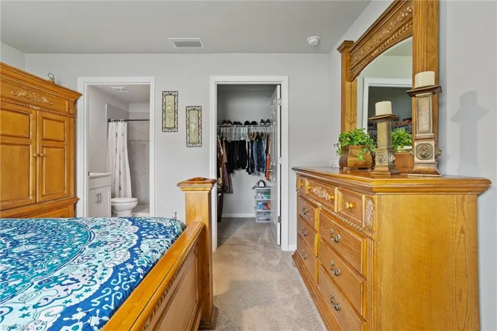 Bedroom with a walk in closet, a closet, light carpet, baseboards, and ensuite bath