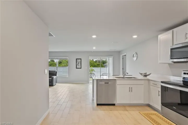 Kitchen with appliances with stainless steel finishes, a sink, light wood-style flooring, white cabinetry, and recessed lighting