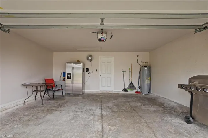 Garage featuring stainless steel fridge with ice dispenser, water heater, a garage door opener, and baseboards