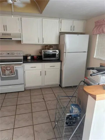 Kitchen featuring light tile patterned floors, white appliances, white cabinets, and under cabinet range hood