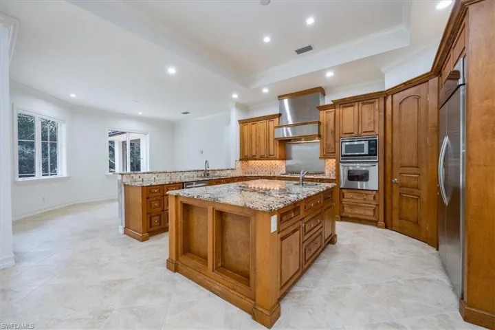 Kitchen with large center island, granite countertops with wood cabinetry and stainless steel appliances.
