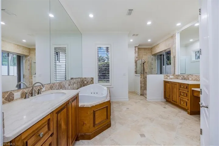 Primary bathroom with tile floor, dual vanities, W/C (not shown), jetted bathtub and shower.