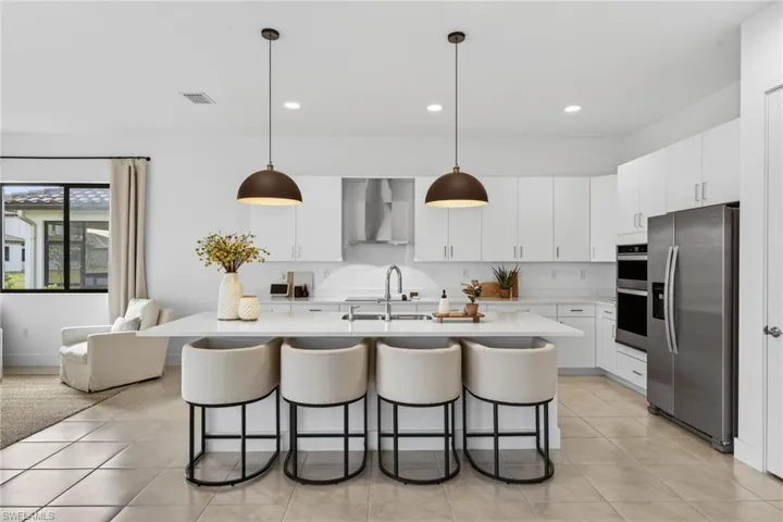 Kitchen with stainless steel appliances, white cabinetry, decorative light fixtures, and a center island with sink