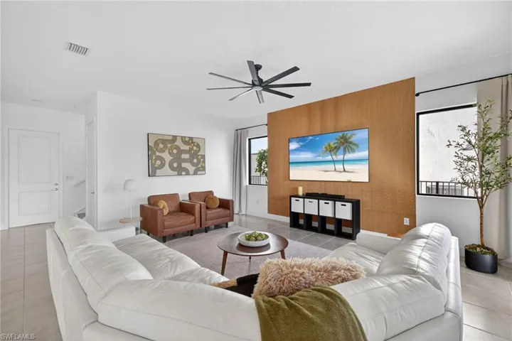 Living area featuring an accent wall, light tile patterned floors, ceiling fan, and wood walls