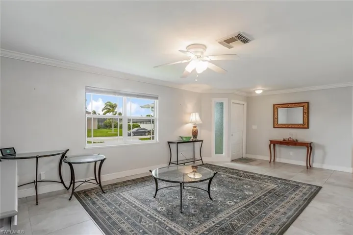 Living room with crown molding, light tile patterned floors, and ceiling fan
