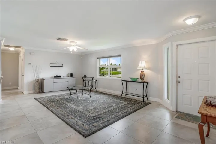 Living room featuring light tile patterned flooring, ceiling fan, and ornamental molding