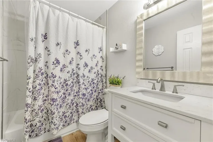 Full bath featuring vanity, shower / tub combo, a textured wall, and light wood-style floors