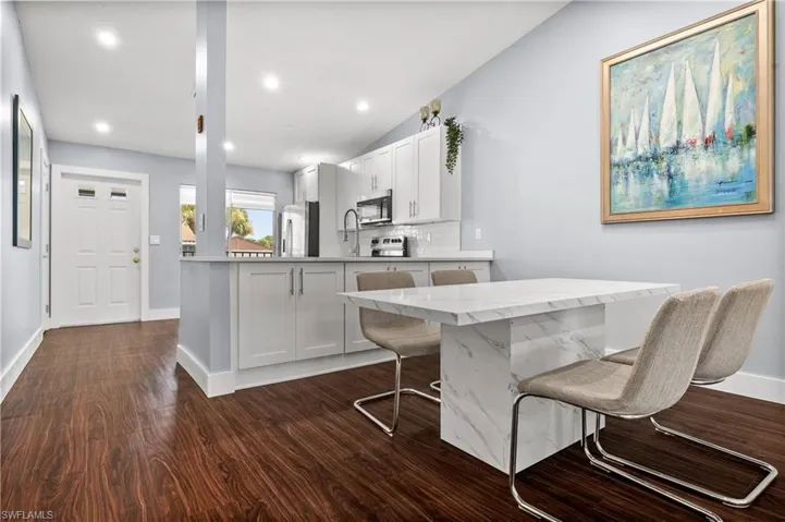 Kitchen featuring white cabinetry, decorative backsplash, lofted ceiling, a breakfast bar, and dark wood-style flooring