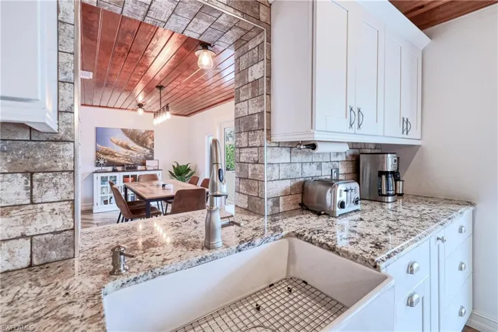 Kitchen featuring white cabinetry, wood ceiling, light stone countertops, pendant lighting, and sink