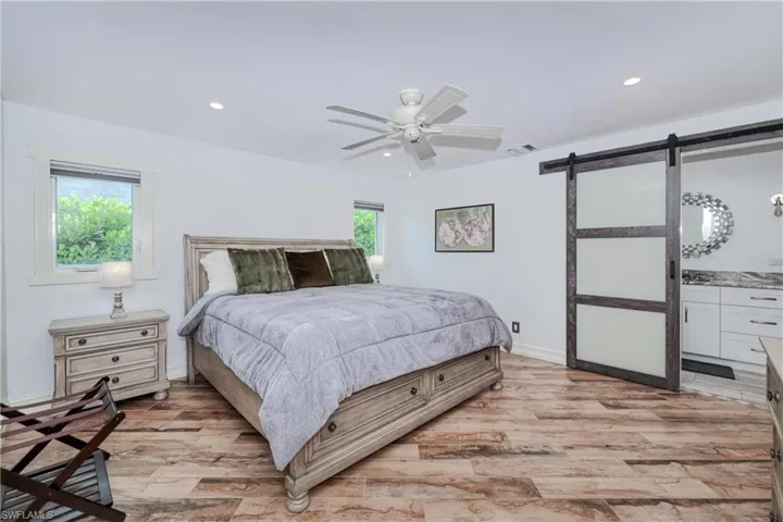 Master Bedroom featuring wood plank tile flooring, ceiling fan, connected bathroom, and a barn door