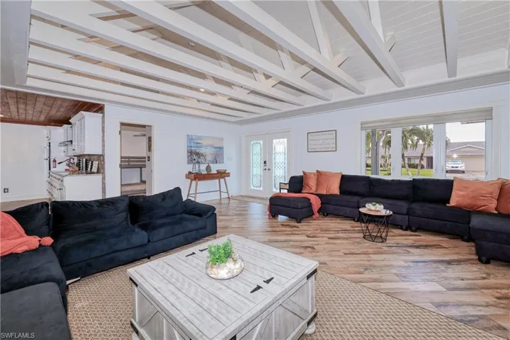 Living room with beam ceiling, a wealth of natural light, french doors, and wood plank tile flooring