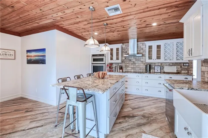 Kitchen with white/gray cabinets, wall chimney range hood, wood ceiling, a kitchen island, and decorative backsplash
