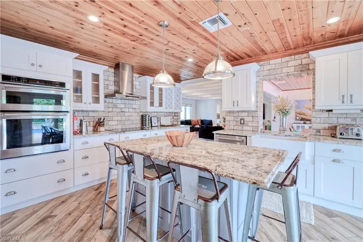 Kitchen featuring tasteful backsplash, stainless steel appliances, attractive range hood,wood plank tile floors, and wooden ceiling