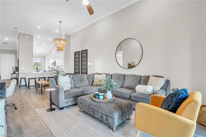 Living room with recessed lighting, light wood-type flooring, ceiling fan with notable chandelier, and crown molding