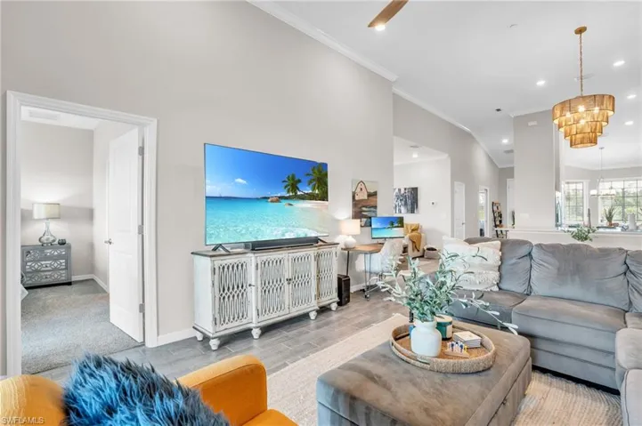 Living room with baseboards, an inviting chandelier, ornamental molding, recessed lighting, and wood finished floors