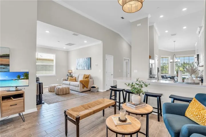 Living room with light wood-style floors, a notable chandelier, crown molding, and a healthy amount of sunlight