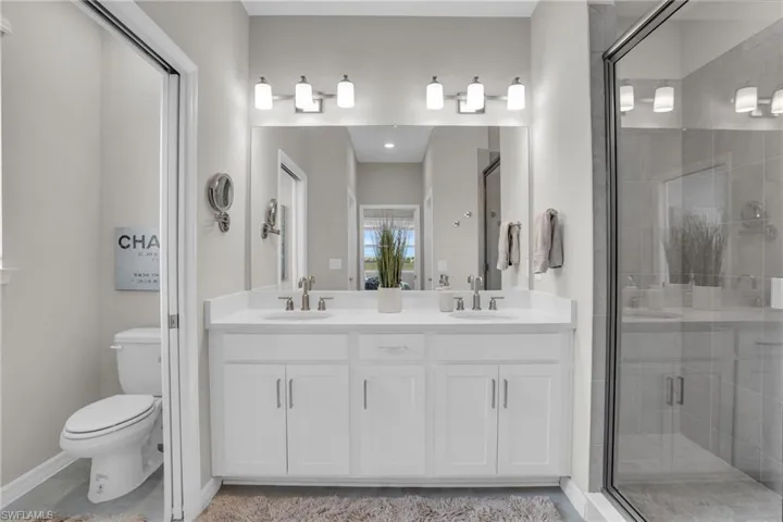 Full bath featuring a sink, toilet, double vanity, and a stall shower