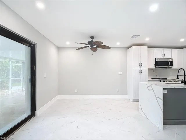 Kitchen with white cabinets, light tile flooring, ceiling fan, and light stone countertops