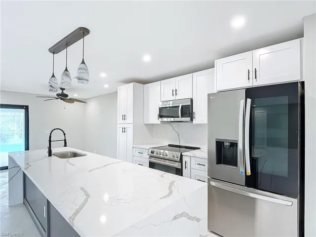 Kitchen featuring ceiling fan, stainless steel appliances, decorative light fixtures, and a kitchen island with sink