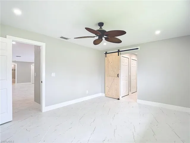 Unfurnished bedroom with a barn door, ceiling fan, and light tile flooring