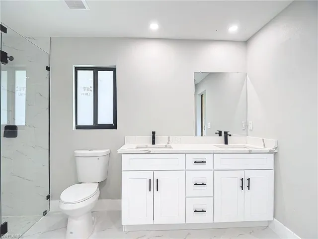 Bathroom featuring oversized vanity, dual sinks, toilet, tile flooring, and a shower with door