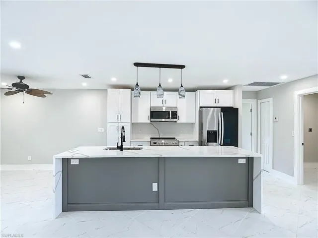 Kitchen featuring a center island with sink, appliances with stainless steel finishes, and light tile floors
