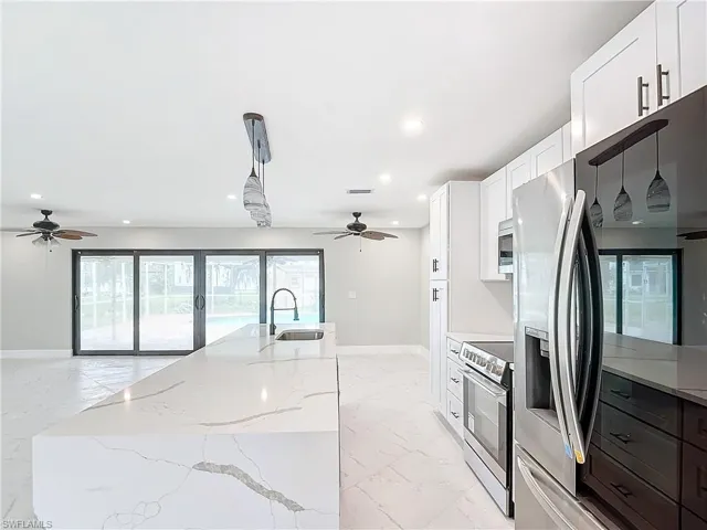 Kitchen with decorative light fixtures, stainless steel appliances, a center island, white cabinets, and light tile floors