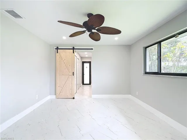 Empty room with a barn door, ceiling fan, and light tile flooring