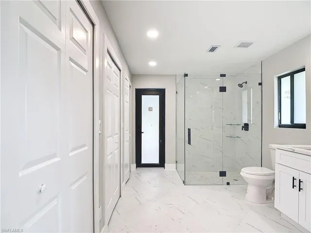 Bathroom with tile floors, a shower with shower door, vanity, and toilet