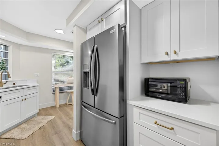 Kitchen with stainless steel fridge with ice dispenser, light wood-style floors, white cabinets, and light stone counters
