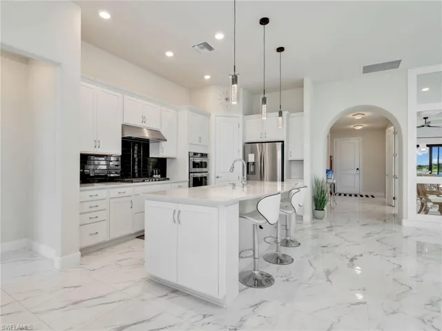 Kitchen with arched walkways, a kitchen breakfast bar, white cabinetry, pendant lighting, and stainless steel appliances