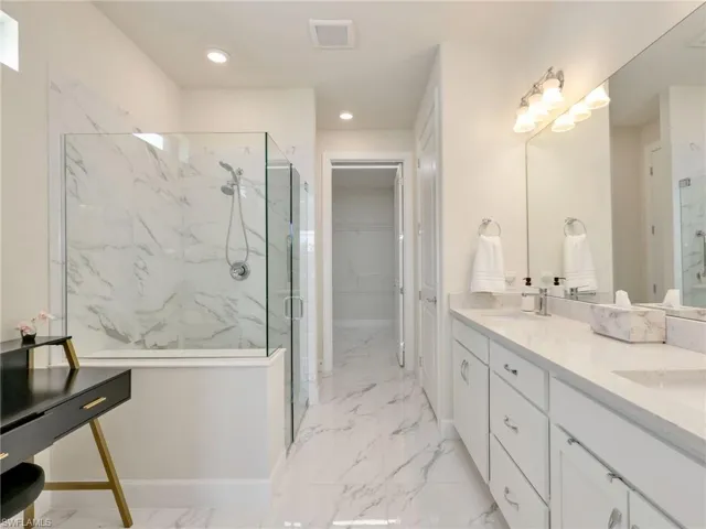 Full bath with a marble finish shower, double vanity, light marble finish flooring, a walk in closet, and recessed lighting