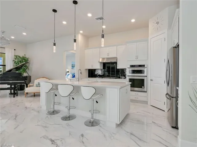 Kitchen with white cabinetry, a breakfast bar, recessed lighting, decorative light fixtures, and a center island with sink