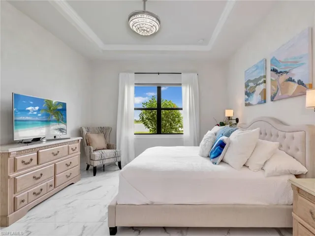 Bedroom with light marble finish floors, ornamental molding, and a tray ceiling