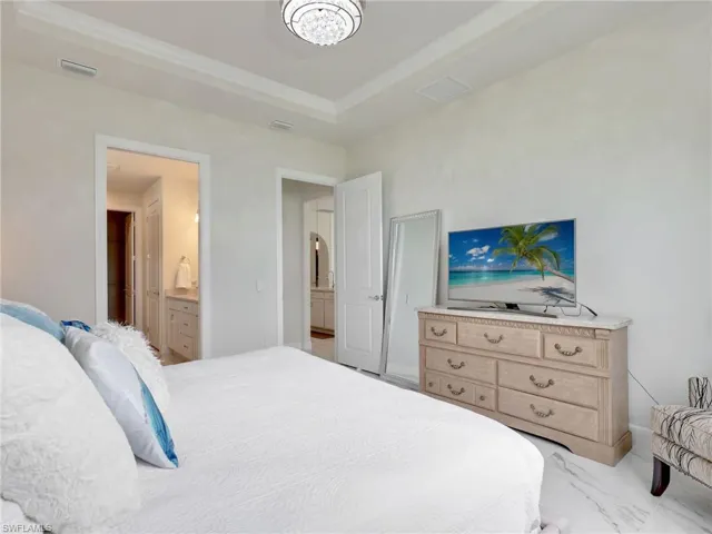 Bedroom with light marble finish floors, connected bathroom, a raised ceiling, and ornamental molding