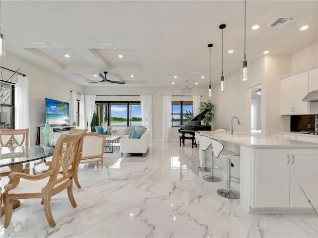 Kitchen featuring white cabinetry, decorative light fixtures, open floor plan, a breakfast bar area, and a kitchen island with sink