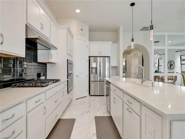 Kitchen featuring arched walkways, white cabinets, light stone counters, hanging light fixtures, and appliances with stainless steel finishes