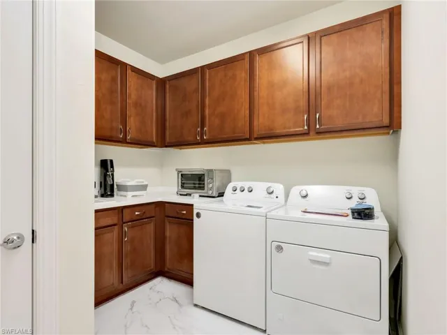 Laundry room featuring light marble finish floors, washing machine and clothes dryer, and cabinet space