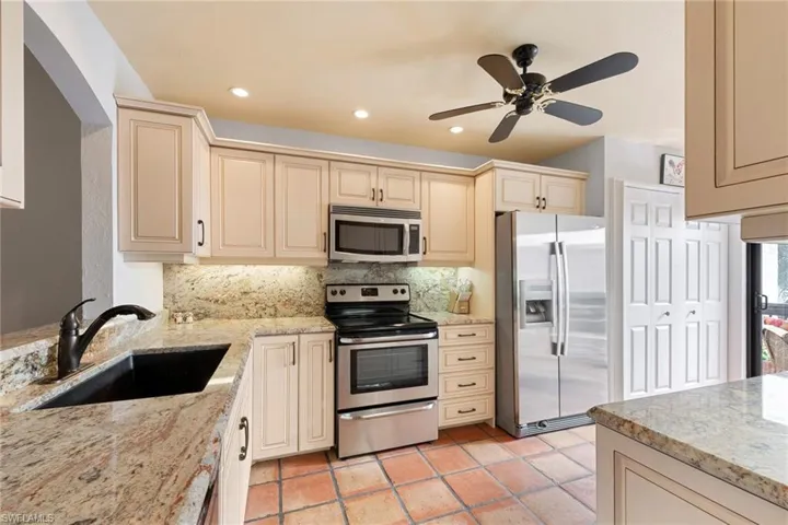 Kitchen featuring stainless steel appliances, light stone countertops, cream cabinetry, recessed lighting, and a ceiling fan
