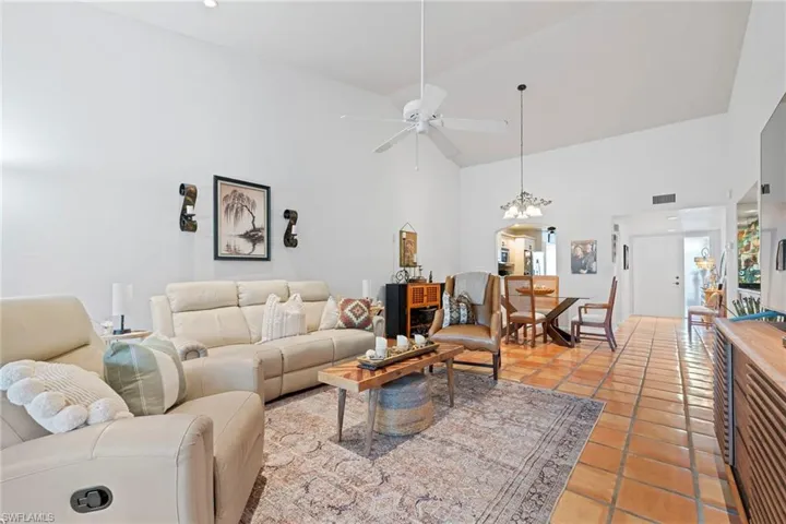 Living room with high vaulted ceiling, ceiling fan, light tile patterned floors, and a chandelier