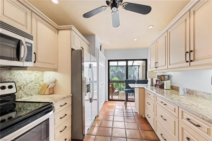 Kitchen featuring stainless steel appliances, cream cabinets, light stone countertops, recessed lighting, and backsplash