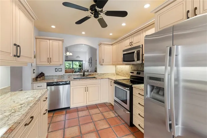 Kitchen featuring appliances with stainless steel finishes, cream cabinetry, light stone counters, arched walkways, and recessed lighting