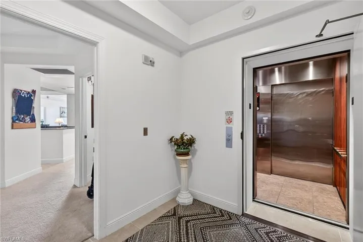 Hallway featuring elevator, light colored carpet, and light tile patterned flooring